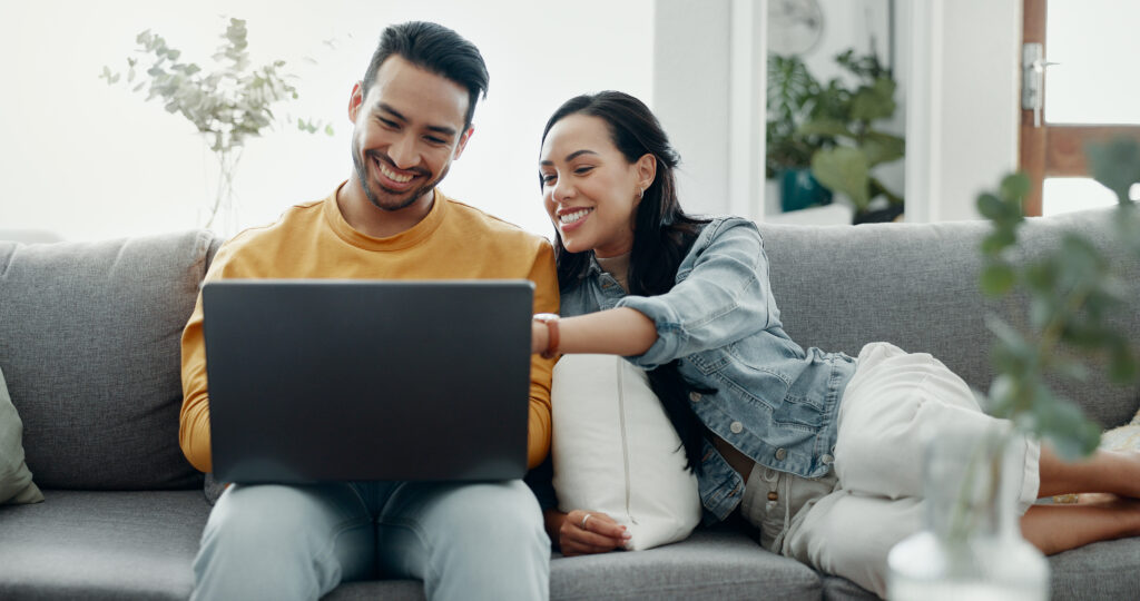 Couple smiling and shopping for a furnace online on a laptop